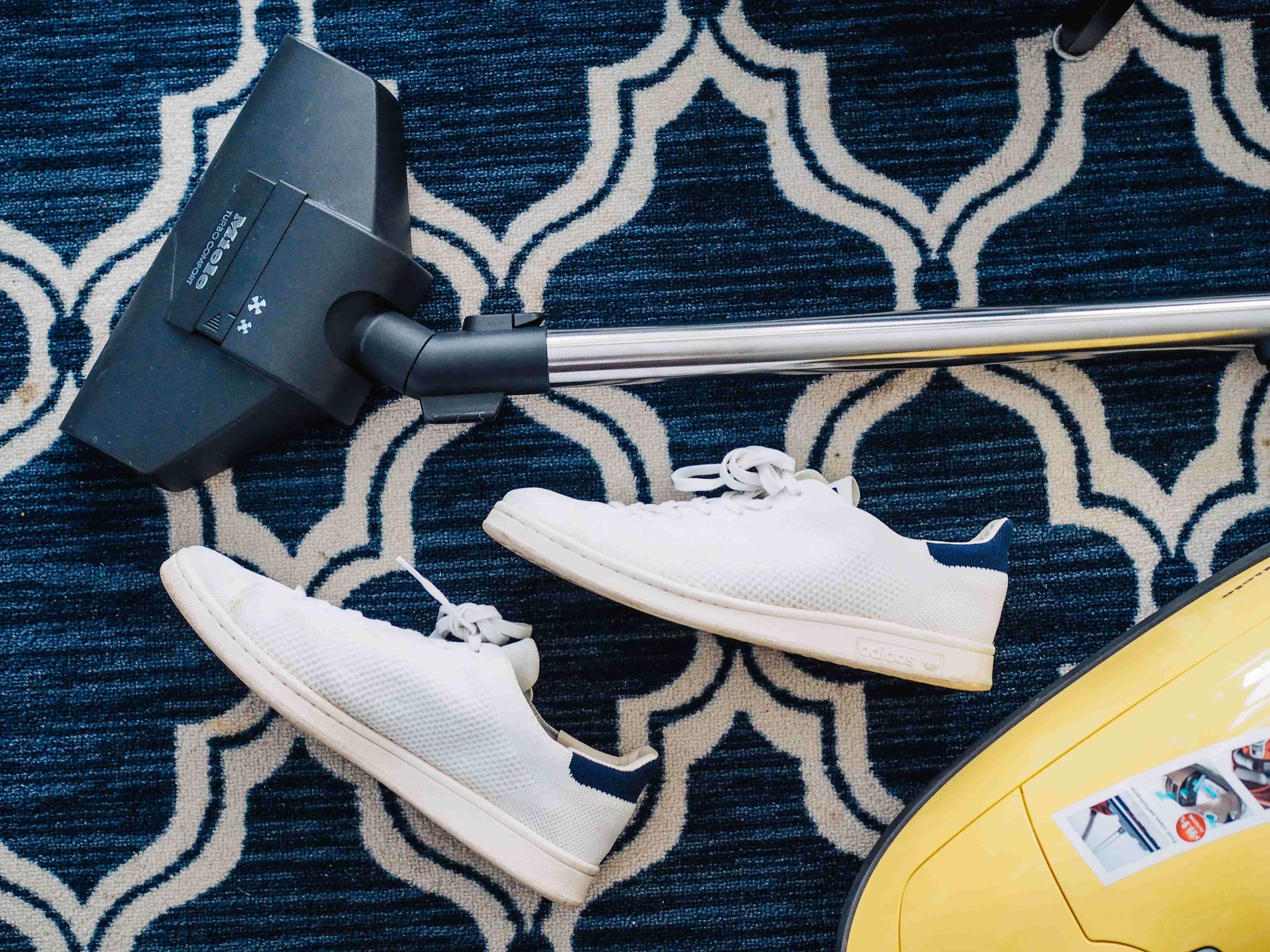 Stofzuigerstang met twee sneakers op een tapijt Stofzuigerstang met twee sneakers op een tapijt