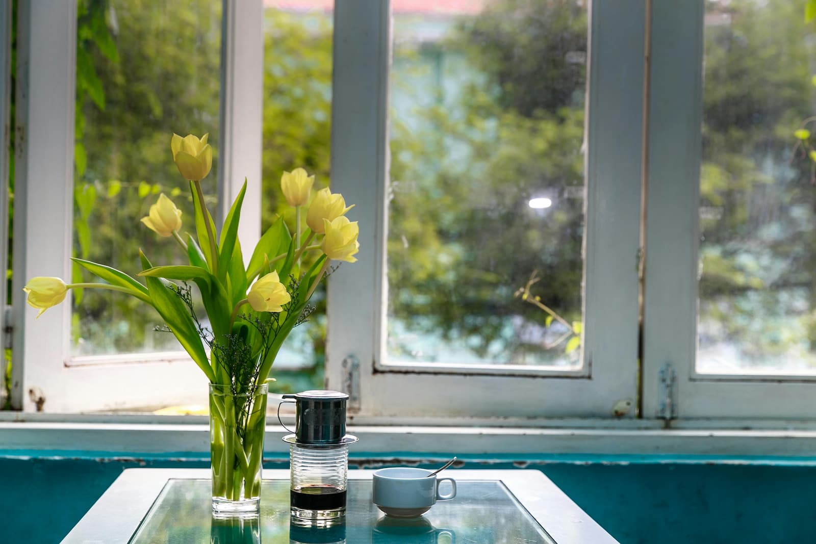 Een raam met dubbelglas en een bos tulpen en een kop koffie op het tafeltje ervoor Een raam met dubbelglas en een bos tulpen en een kop koffie op het tafeltje ervoor