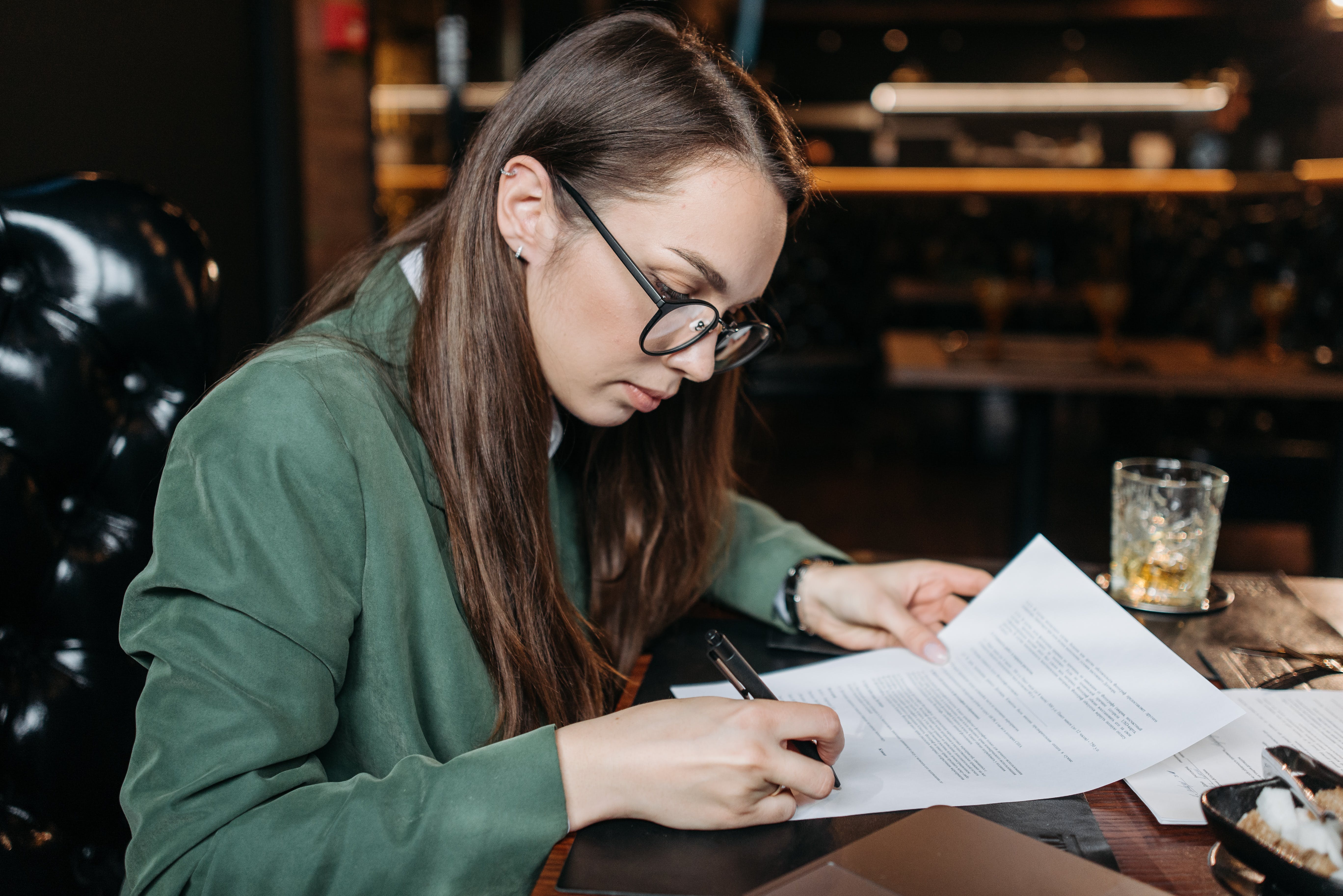 Een vrouw met een bril en een groen jasje aan tekent een contract Een vrouw met een bril en een groen jasje aan tekent een contract